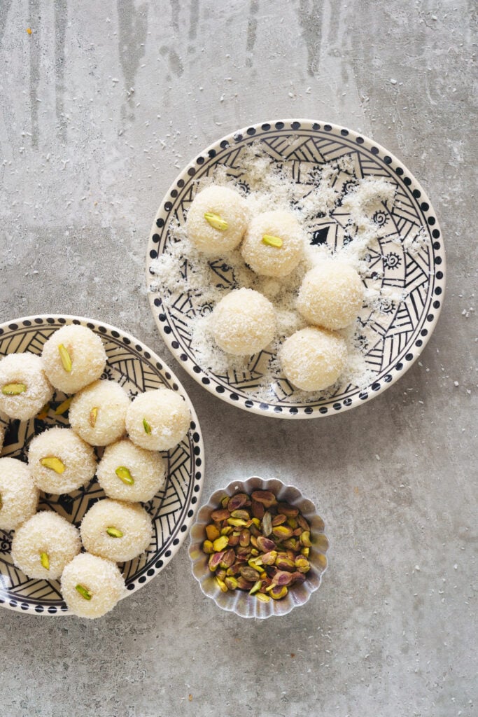 Coconut laddus being rolled in the dried coconut, topped with a sliver of pistachio