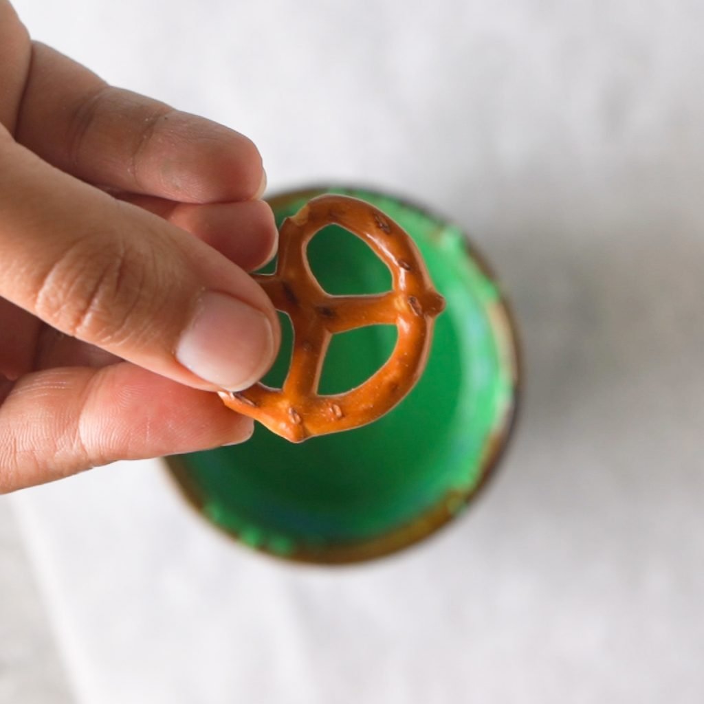 Dipping Pretzels into green candy melt to make Halloween Alien Pretzel Treats