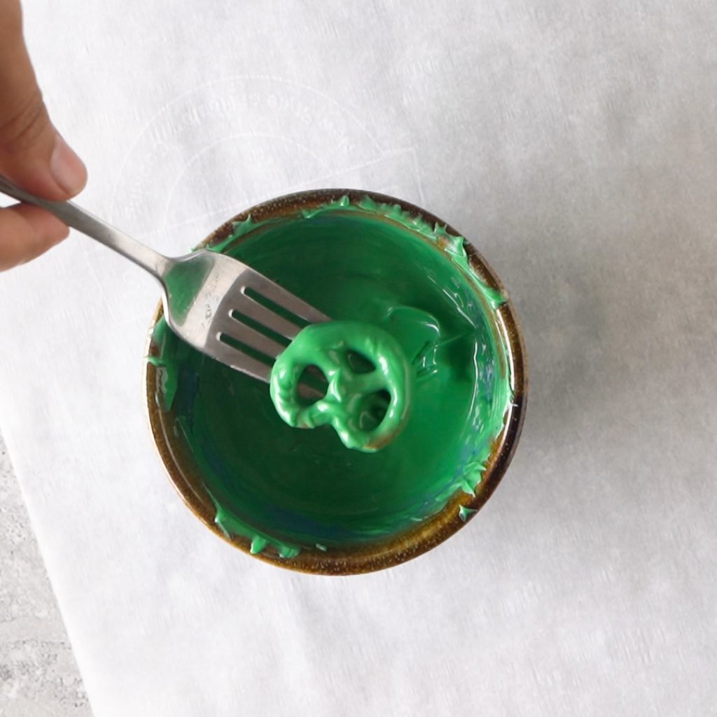 Dipping Pretzels into green candy melt to make Halloween Alien Pretzel Treats