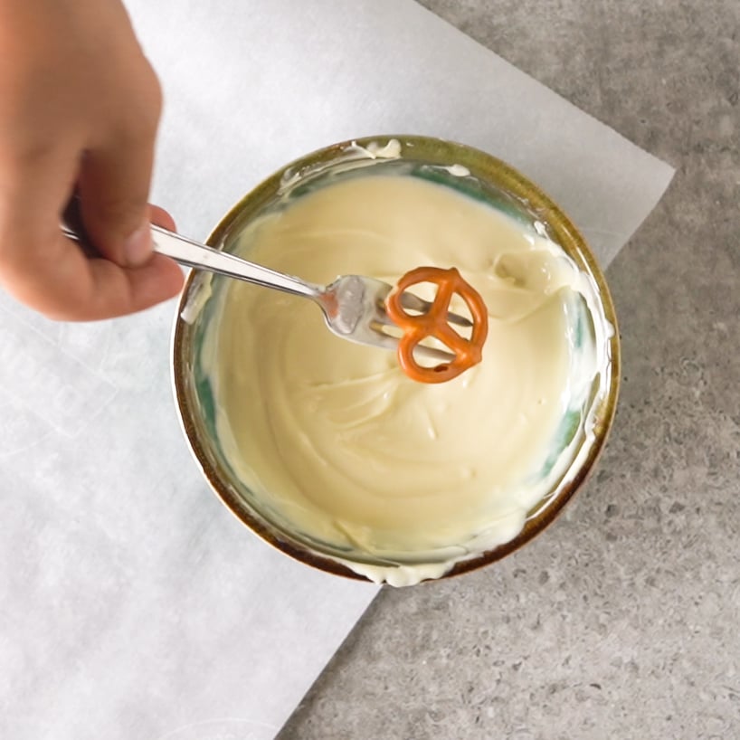 Dipping a mini pretzel in the melted chocolate with a fork