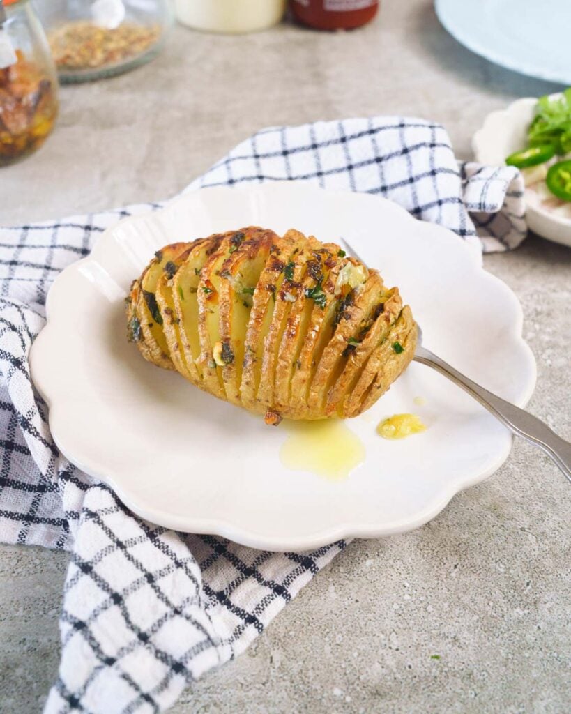 Side view of hasselback potatoes with butter on it on top of a white small plate