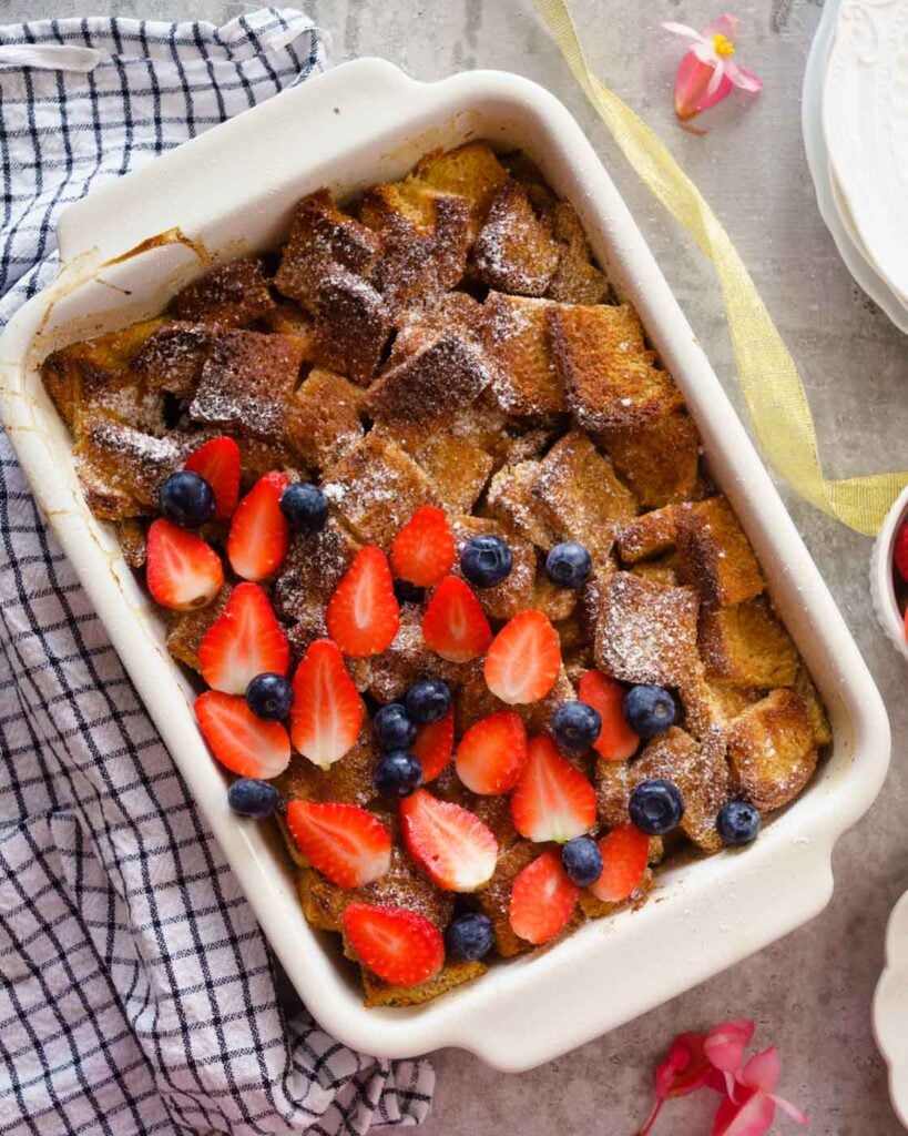 French Toast casserole made with brioche bread in a 9*13 inches baking dish, topped with powdered sugar , strawberries and blueberries