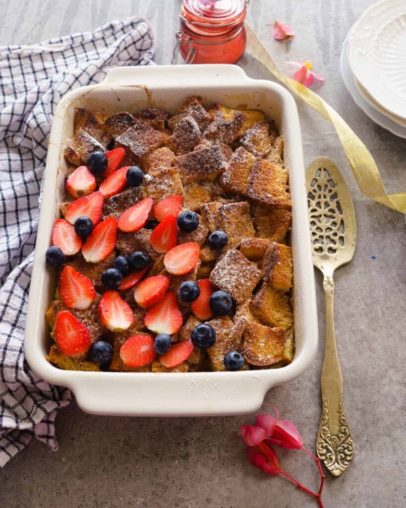 Baked Brioche french toast in a white baking dish with a bronze cake spoon on the side