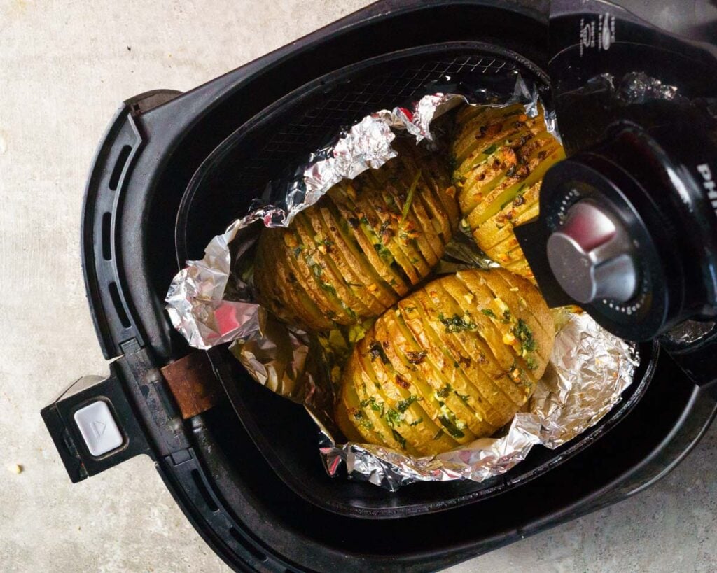 Cooked Browned Hasselback Potatoes on a foil inside the air fryer basket after being cooked.