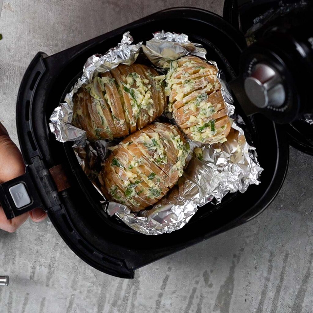 Buttered raw Hasselback Potatoes on a foil inside the air fryer basket ready to be cooked