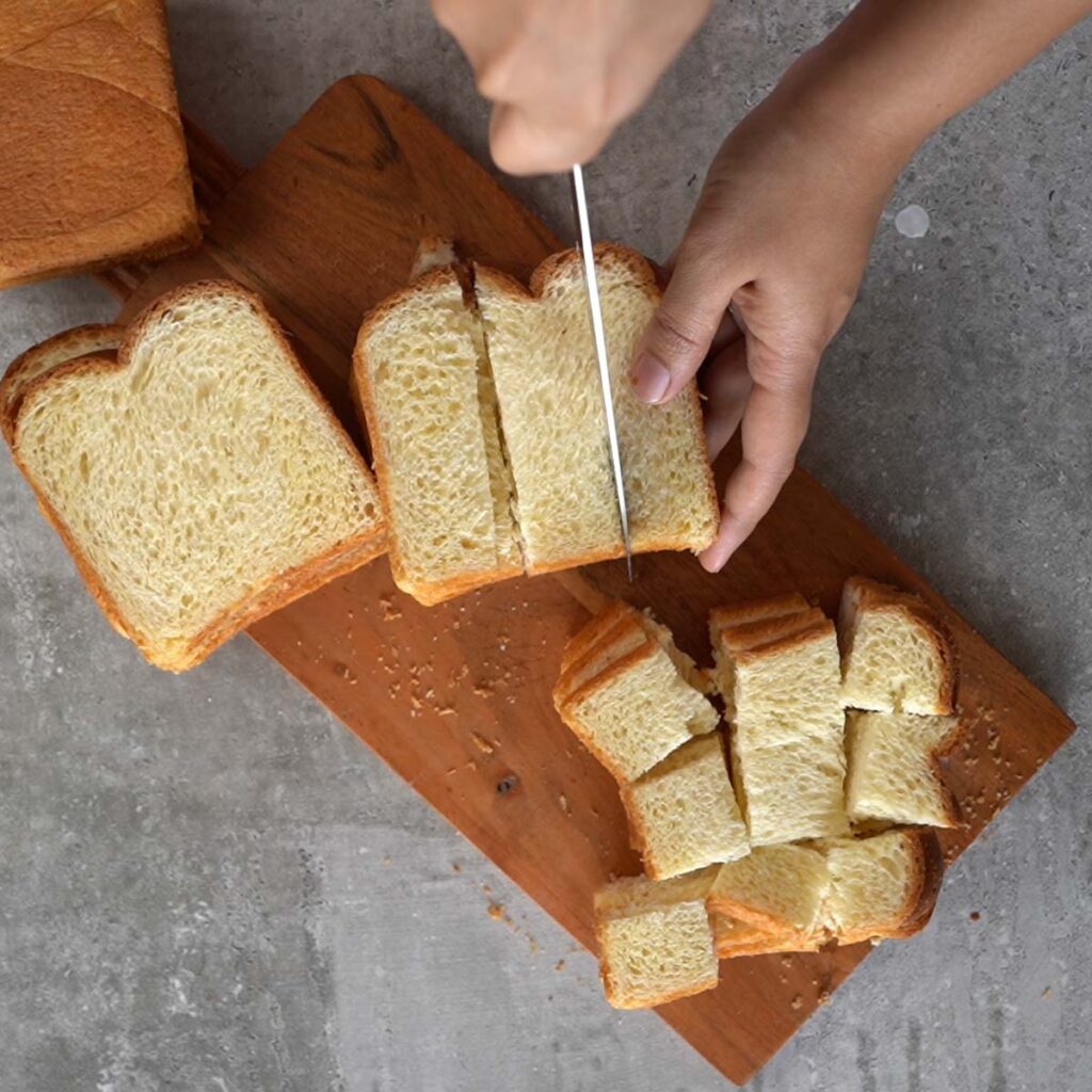 Cutting the brioche bread into cubes on a wooden cutting board