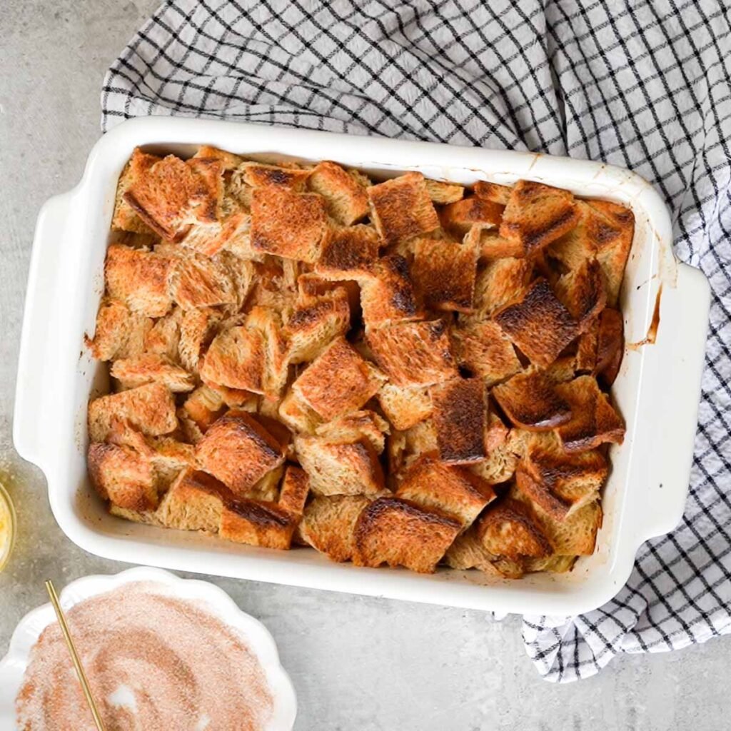 Baked French toast casserole inside a white baking dish with a white and black checkered tea towel