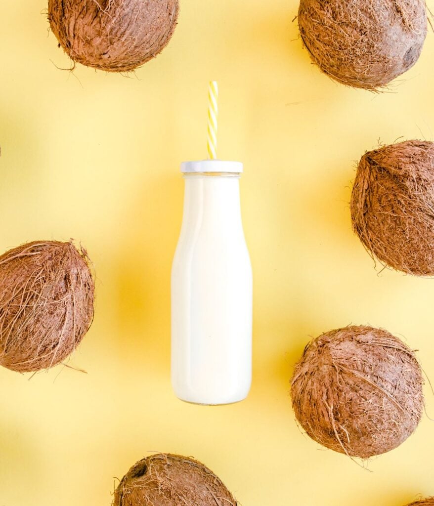 coconut milk in a bottle on yellow background surrounded with coconuts