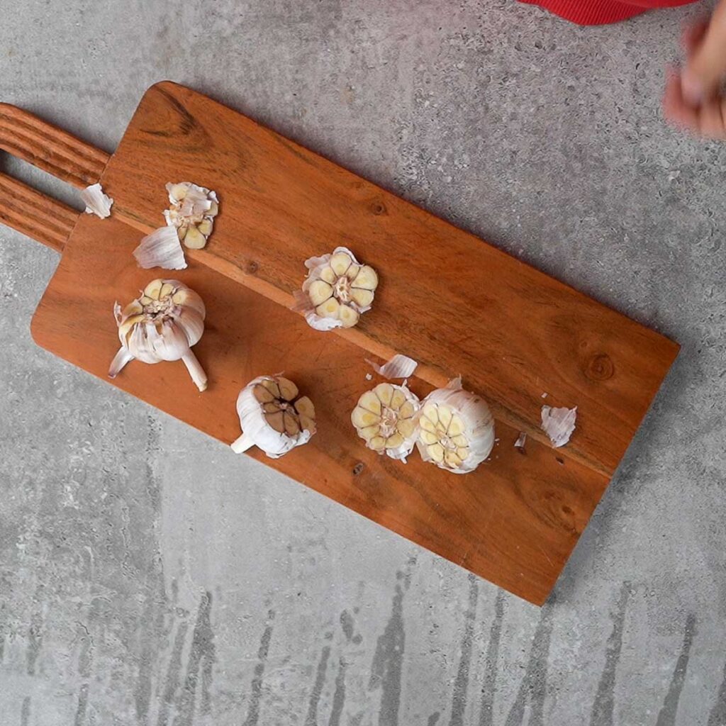 Garlic pods with their tops cut off on a wooden cutting board