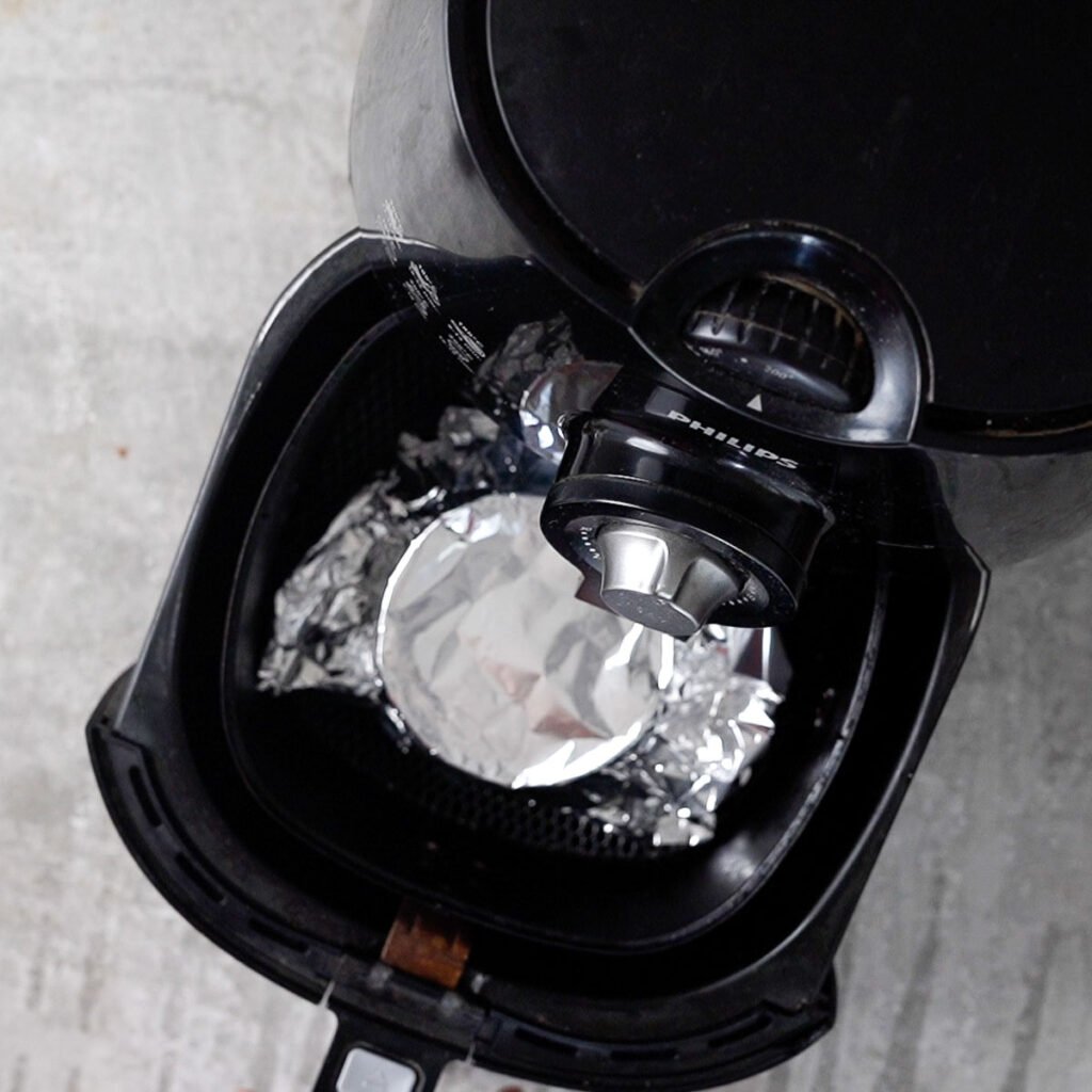 Peeled cloves in a ramekin covered with foil going inside the air fryer.