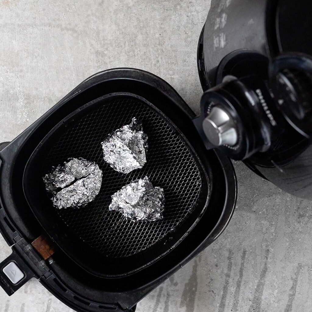 Aluminum foil wrapped garlic in the air fryer ready to be roasted