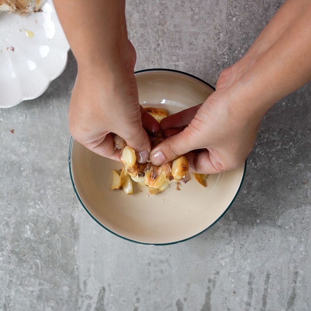 Soft garlic being squeezed out of its peel with hands