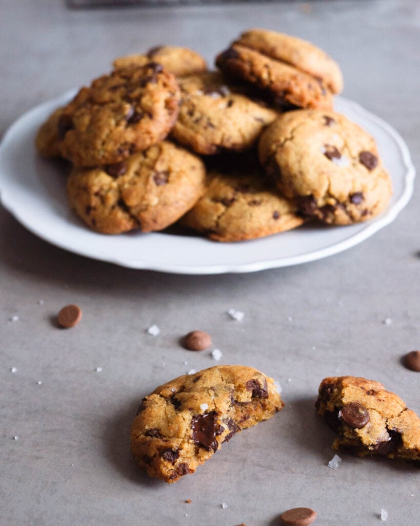 Broken chocolate chip cookie and a plate full of them behind.