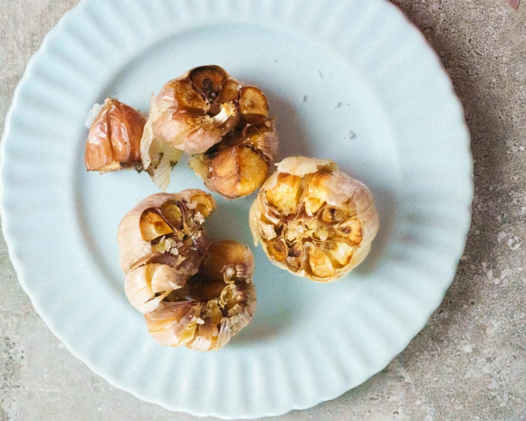 Whole roasted garlic cloves on a blue plate.