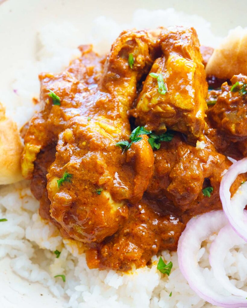 chicken vindaloo on top of rice with onions and bread