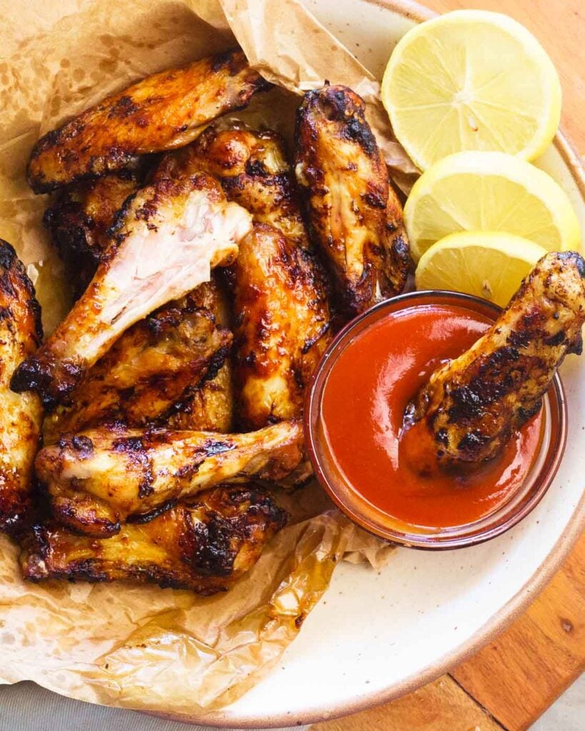 Air fryer chicken wings in a white bowl, lined with brown paper, served with ketchup and lemon slices