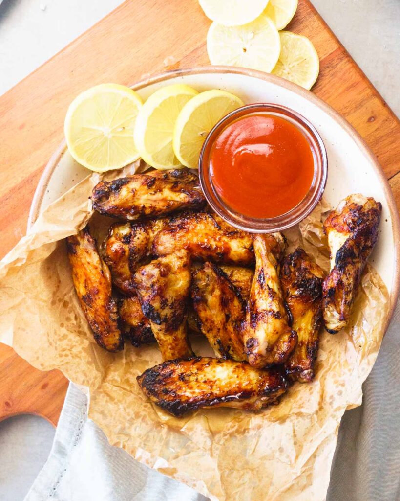 Air fryer chicken wings in a white bowl, lined with brown paper, served with ketchup and lemon slices