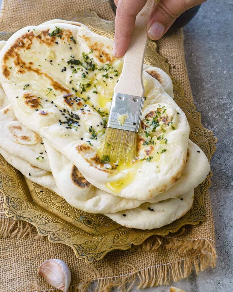 Soft pillowy butter garlic Naans stacked one on top of the other with garlic butter being brushed on them