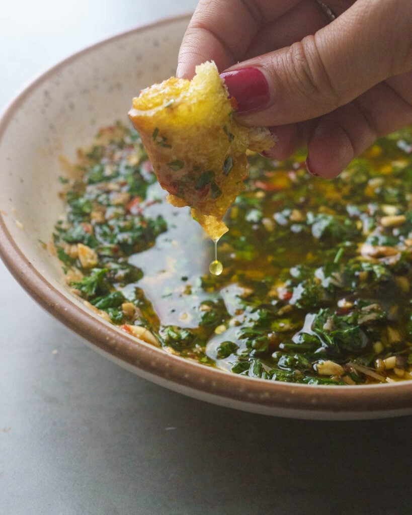 Olive Oil & Balsamic Herb Bread Dip in a white bowl with a piece of bread dripping with oil