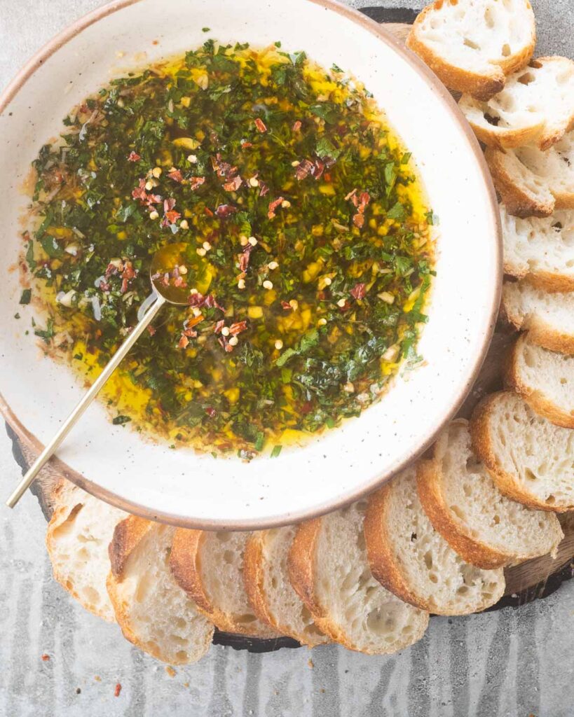 Olive Oil & Balsamic Herb Bread Dip in a white bowl with sliced bread all around it
