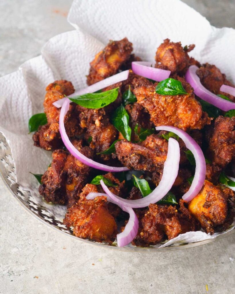 Chicken 65- indian fried chicken in a silver bowl with curry leaves and onion