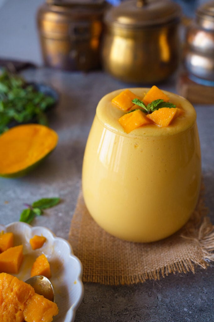 A glass full till the brim with Mango lassi with Mango pieces and a sprig of mint
