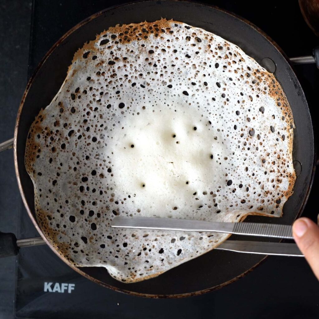 Appam being listed out of the appam pan with tongs