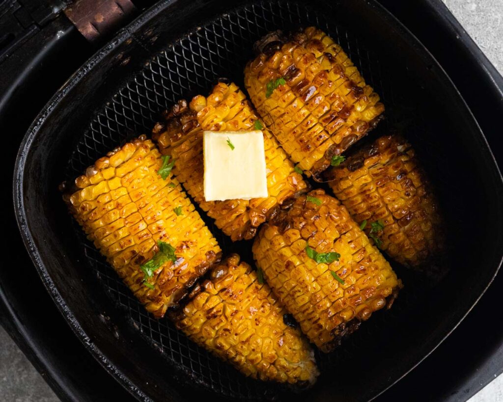 Grilled corn with a square of butter, inside air fryer basket, garnished with cilantro