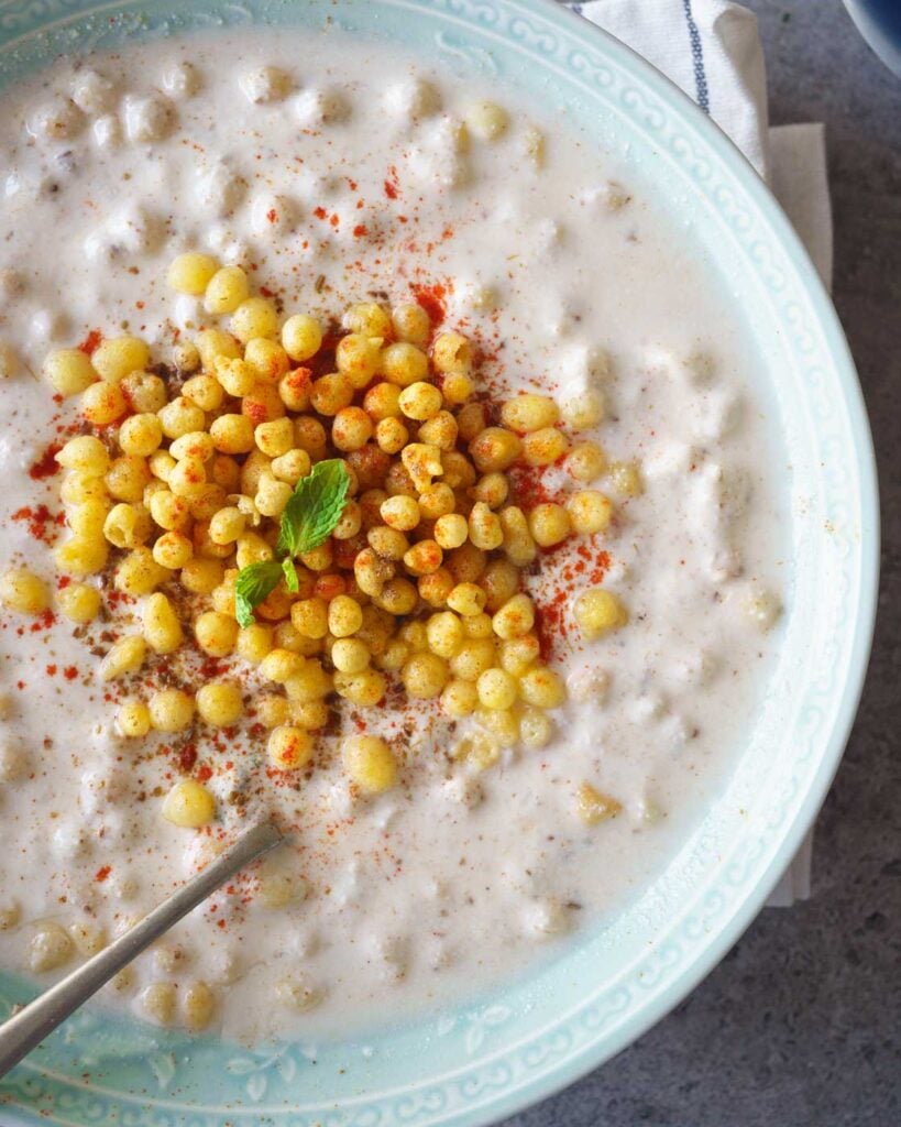 Boondi Raita- Indina yogurt sauce in a green bowl with a sprig of  mint on top