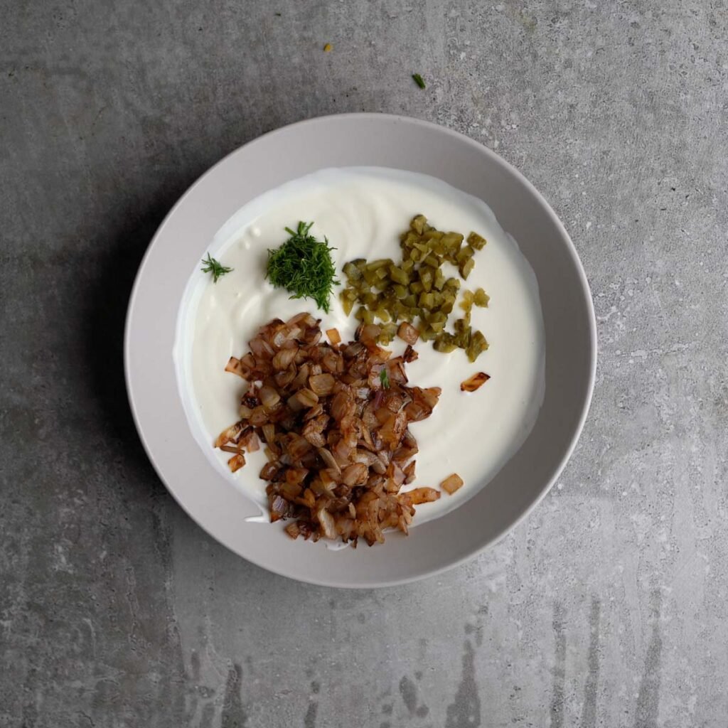 caramalised onion, dill leaves and chopped pickle on top of whisked yogurt and mayonnaise