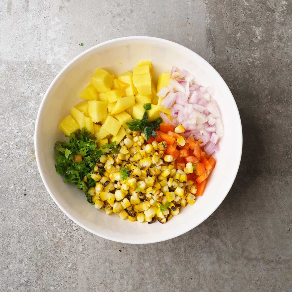 Diced up mango, grilled corn, red bell pepper, onions and cilantro in a white bowl