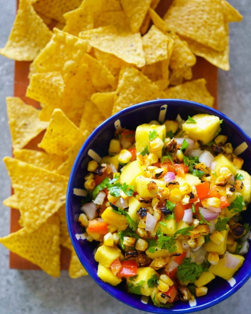 Mango, grilled corn, cilantro, red bell pepper salsa in a white and blue bowl, served with tortilla chips