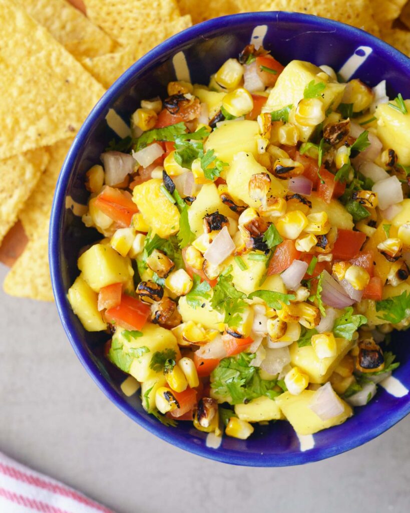 Mango, grilled corn, cilantro, red bell pepper salsa in a white and blue bowl, served with tortilla chips