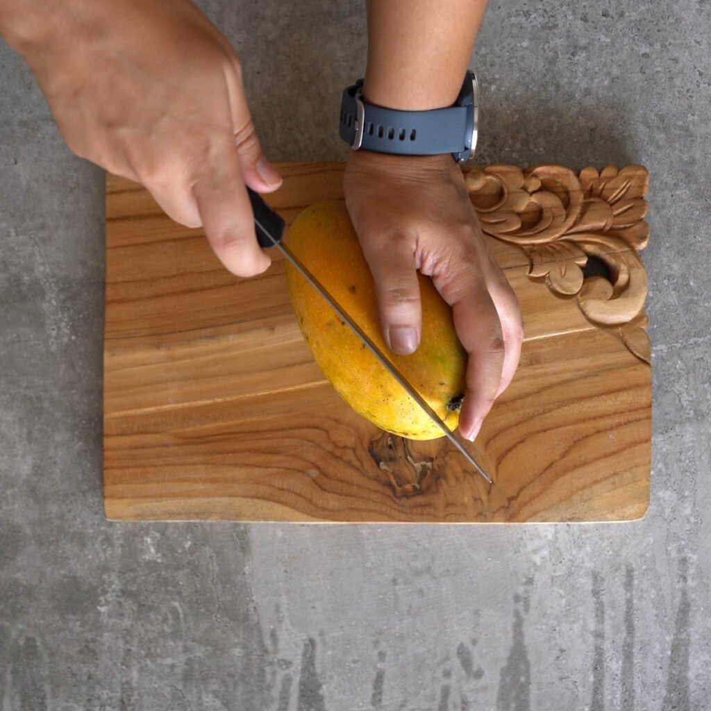 Cutting a Mango with a knife and a wooden cutting board