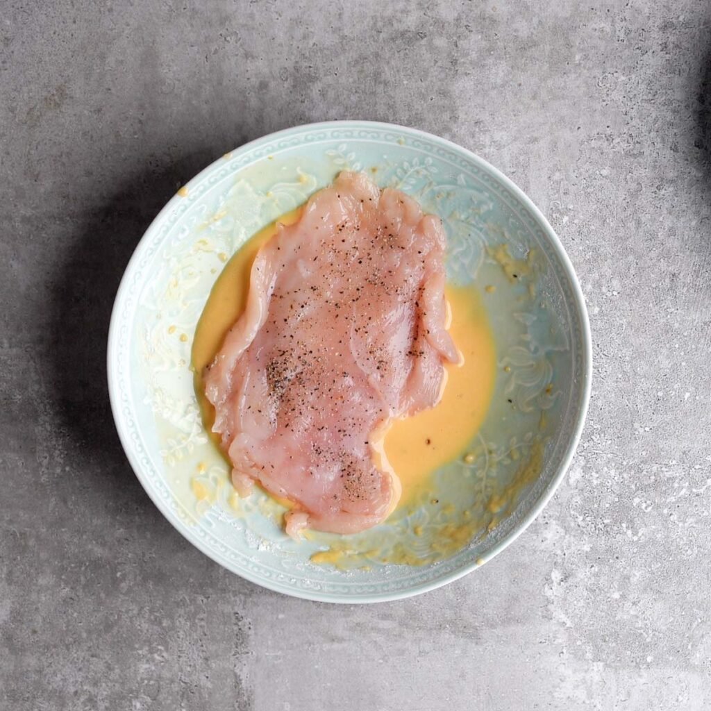 Chicken fillet with salt and pepper, being dipped into the wet batter made of eggs, flour and garlic powder