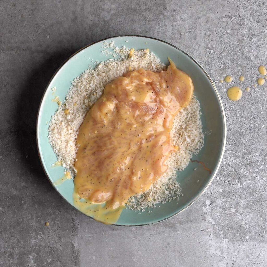 Chicken breast thats been coasted with the wet mixture, in a bowl with panko bread crumbs