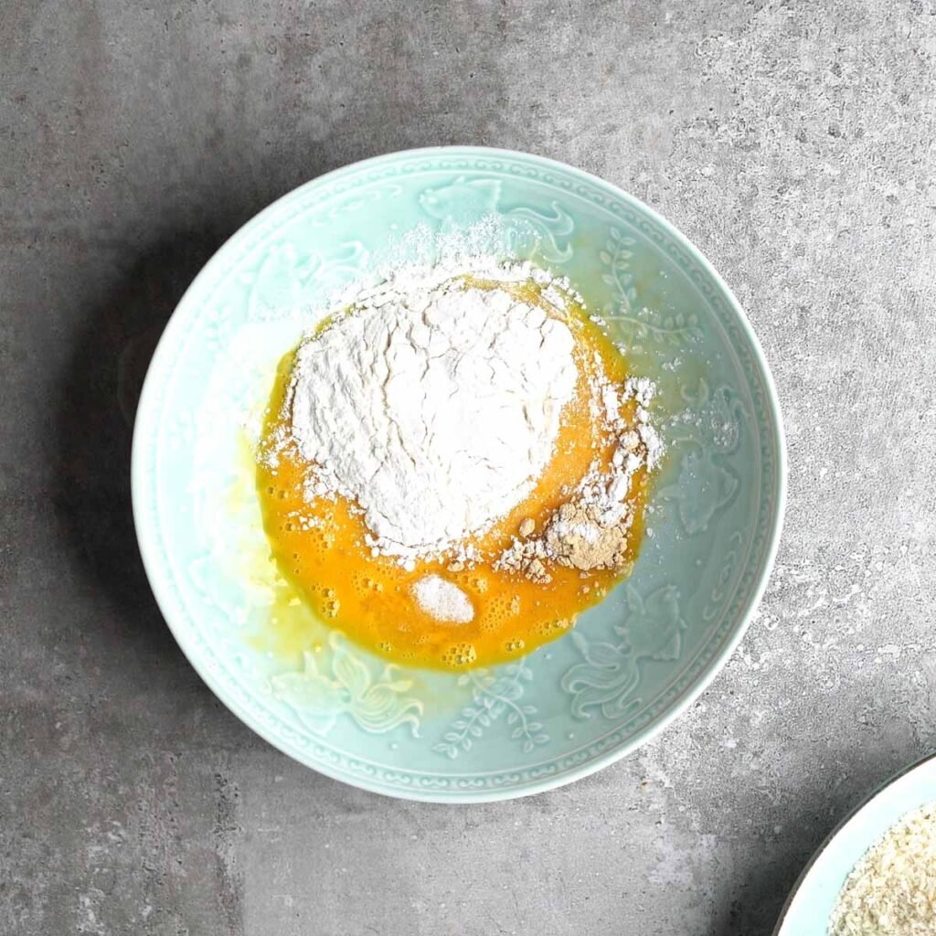 Whisked egg, flour, salt & garlic powder in a light green bowl before mixing.