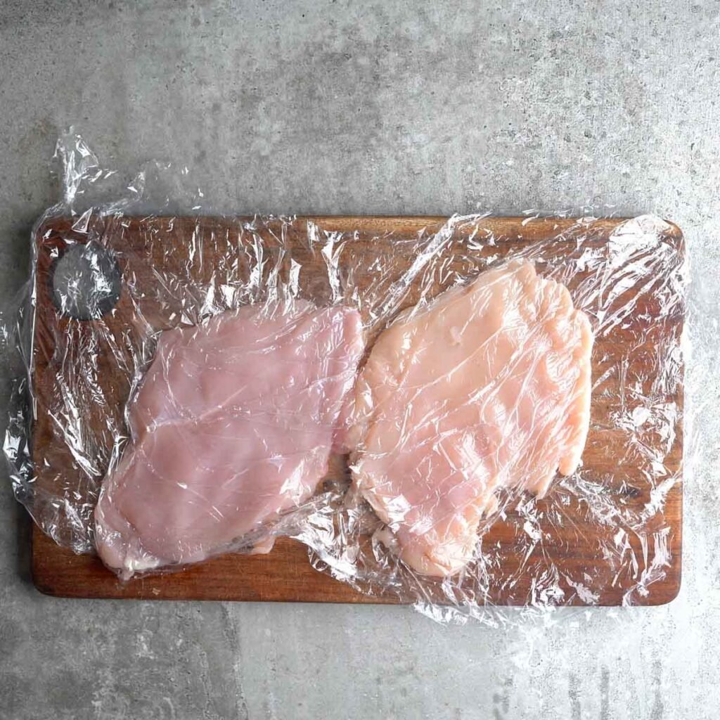 2 chicken breasts on a cutting board lined with plastic wrap; pounded to ½ inch thickness