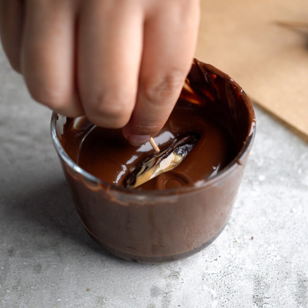 Stuffed date being dipped into melted chocolate