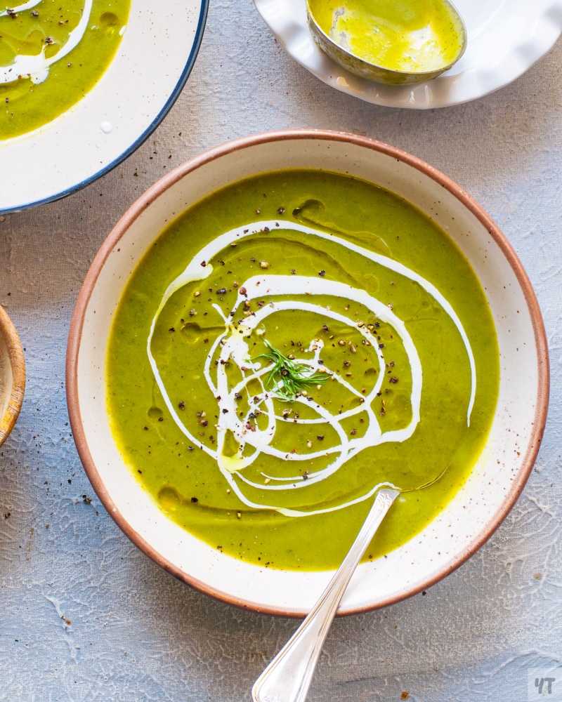 Bright green Zucchini Soup in a white bowl with a drizzle of olive oil and cream.