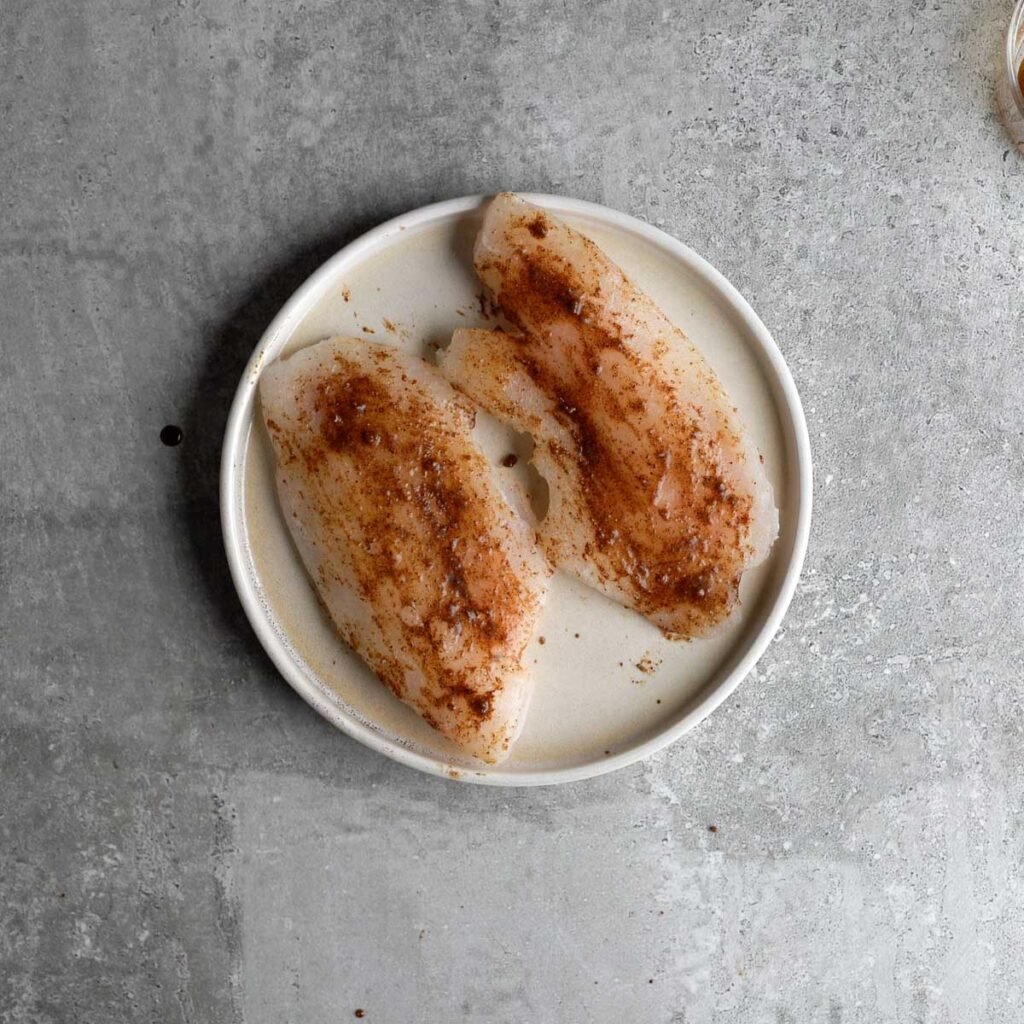 Two Frozen tilapia fillets brushed with spice mix, ready to be ari fried.