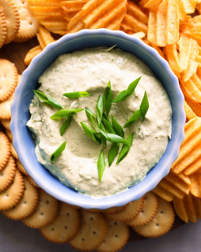 Green onion dip served in a blue bowl, along with ritz crackers and potato chips