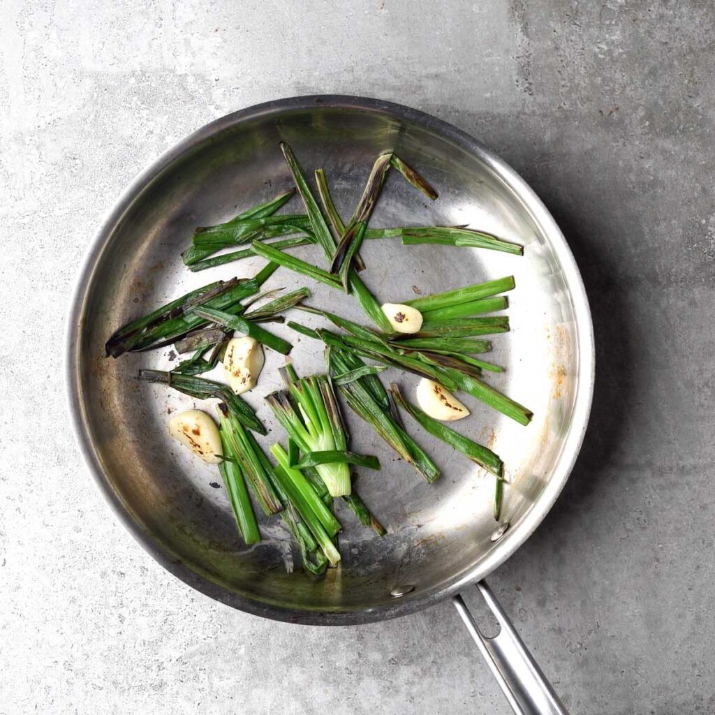 Charred fresh green onions and garlic in a pan