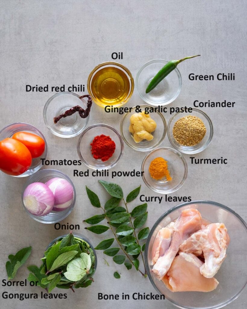 Ingredients needed to make Gongura chicken curry - green chili, coriander powder, turmeric, chicken, curry leaves, sorrel leaves, onion, tomatoes, red chili powder, ginger garlic paste, red dried chili and oil.