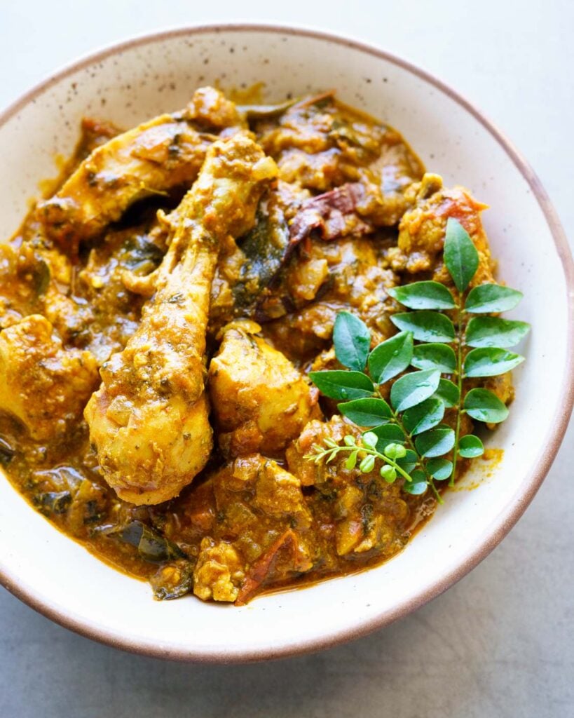 Gongura chicken curry in a white bowl with three sprigs of curry leaves