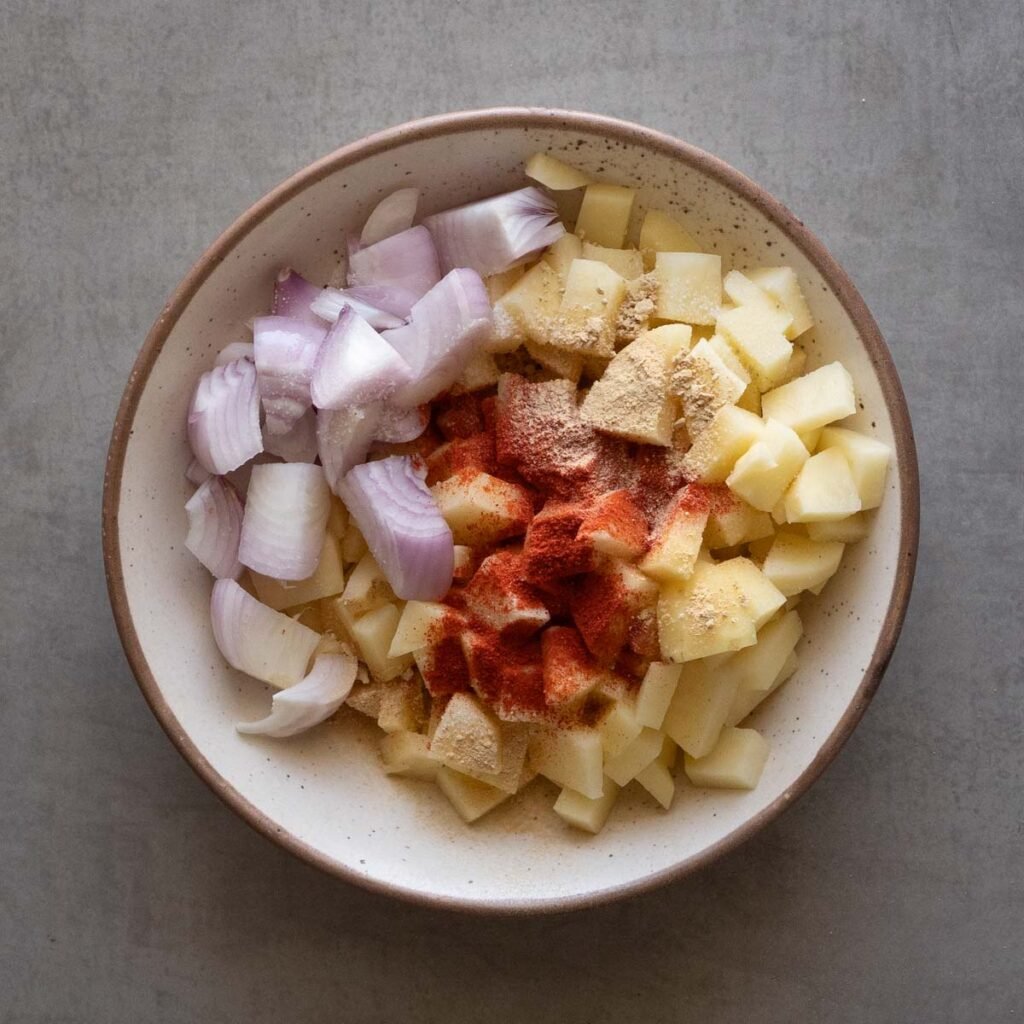 potatoes and onion in a bowl with garlic powder, salt and chili powder