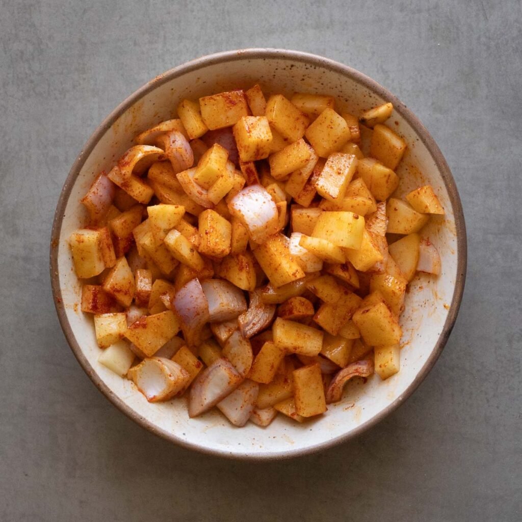 potatoes and onion in a bowl with garlic powder, salt and chili powder