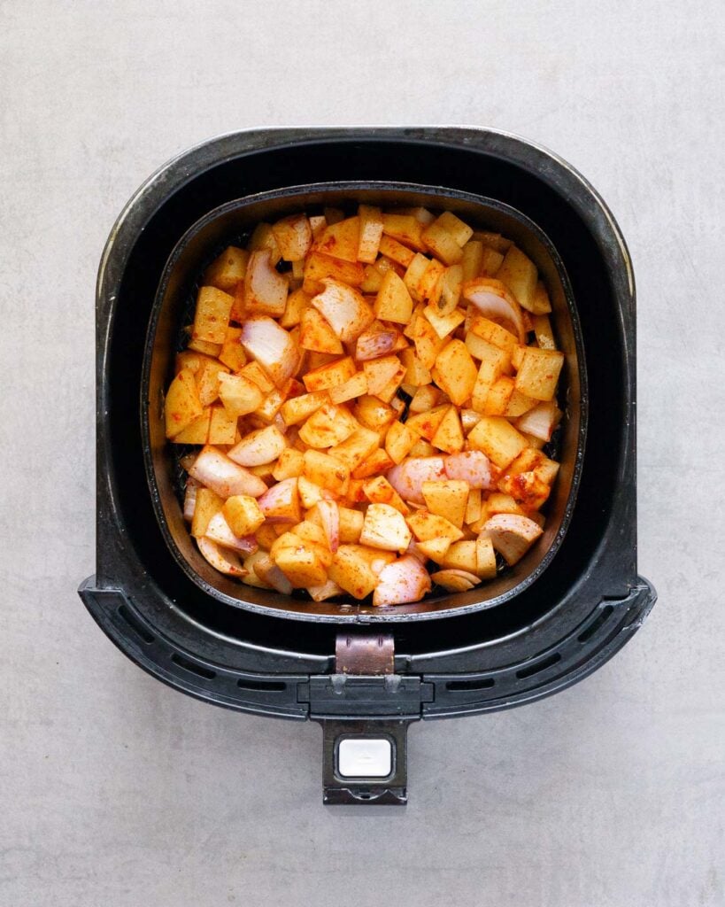 seasoned potatoes and onion in air fryer inner basket