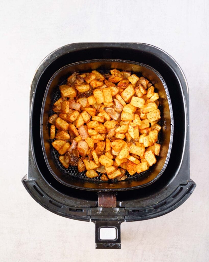 Crispy air fryer potatoes and onions in the air fryer basket.