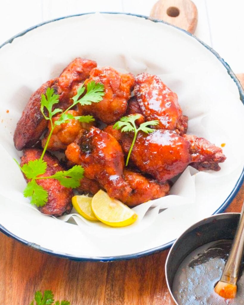 Chicken wings tossed in a spicy thai chili sauce on a white plate with a blue rim, garnished with cilantro